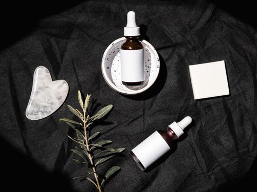 Free Stylish flat lay of skincare serum bottles with gua sha tool and leaves on a dark textile background. Stock Photo
