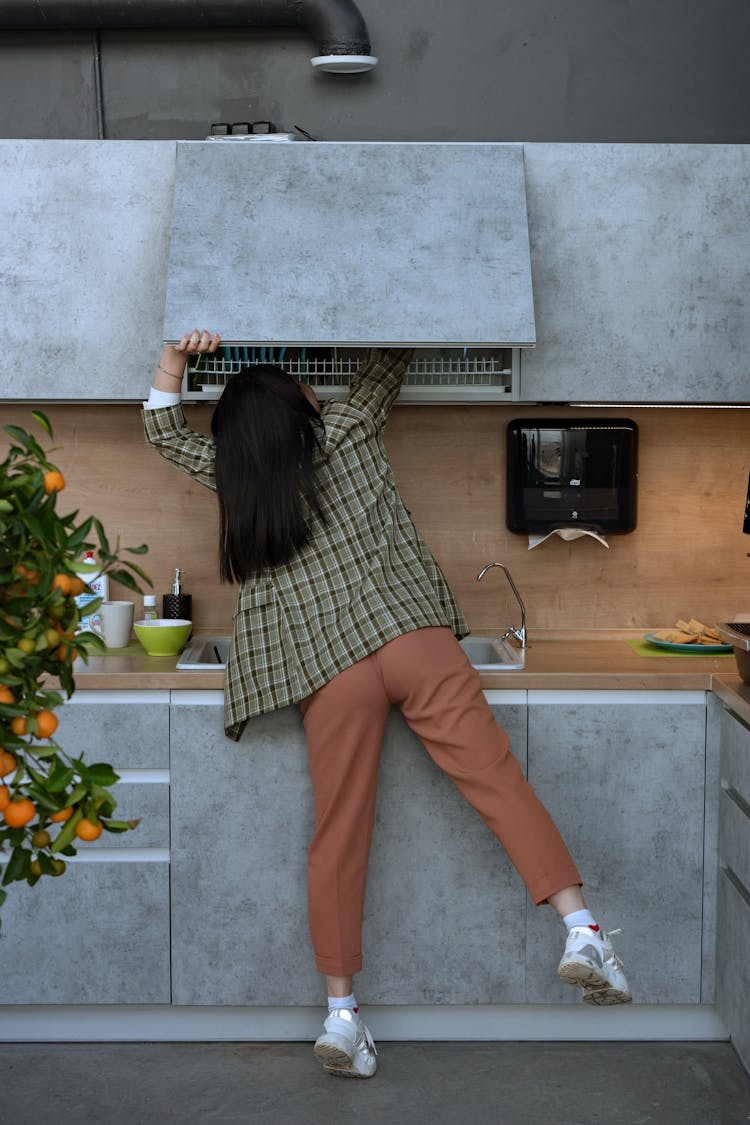 Woman Reaching For Something Inside The Kitchen Cabinet