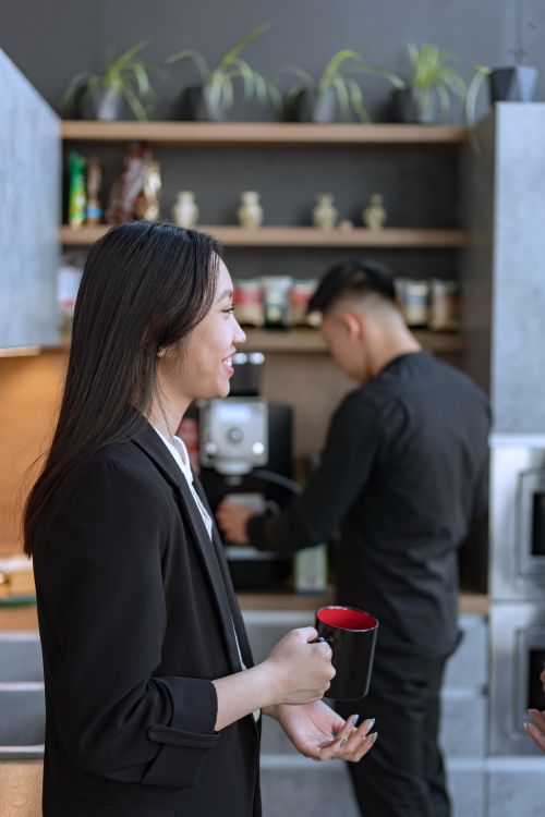 Free Two colleagues enjoying a coffee break in an office kitchen setting, sharing smiles and conversation. Stock Photo
