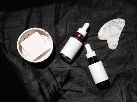 High-angle view of skincare products including serums, gua sha, and bar soap on a dark fabric backdrop.
