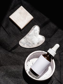 Flat lay of skincare products, including serum bottle and gua sha tool, on black fabric.