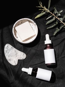 Arrangement of skincare products with gua sha, soap, and serum bottles on a dark textile backdrop.