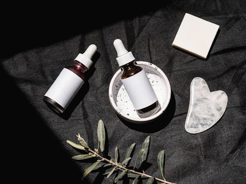 Free Brown Glass Bottles on Black Textile Beside Gua Sha and Bar Soap Stock Photo