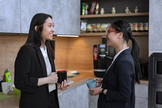 Two businesswomen enjoying a casual conversation over coffee in an office kitchen.