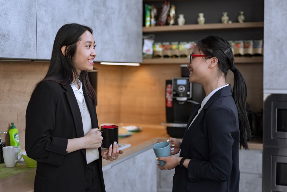 Two people in a casual conversation over coffee in a workspace