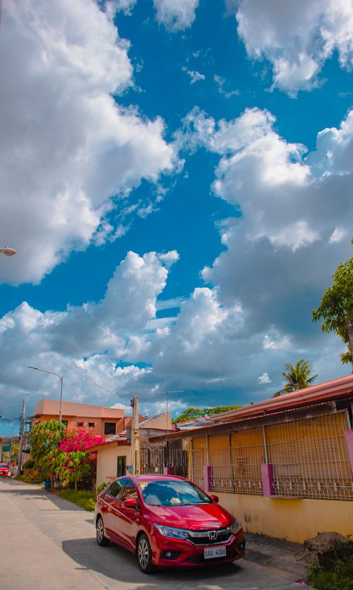 Free Red car parked on a quiet residential street under a bright blue sky with fluffy clouds. Stock Photo