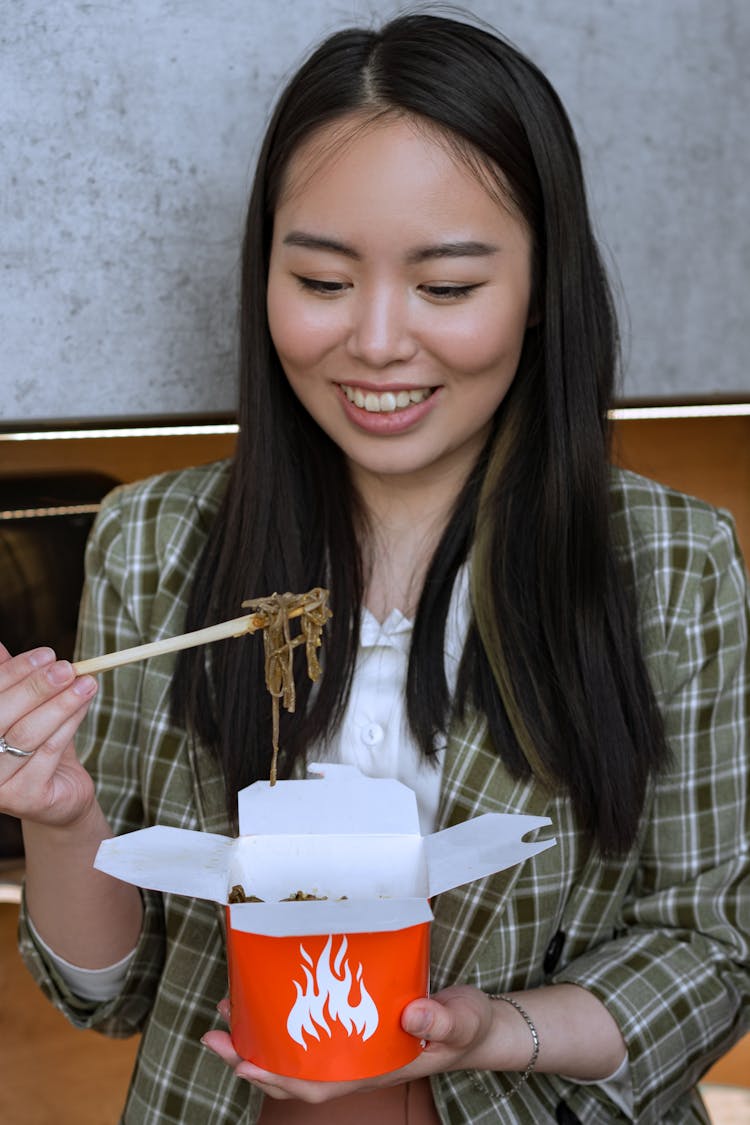 A Woman Eating Noodles From A Takeout Box