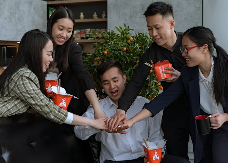 A Group Of People Stacking Hands While Holding Takeout Boxes