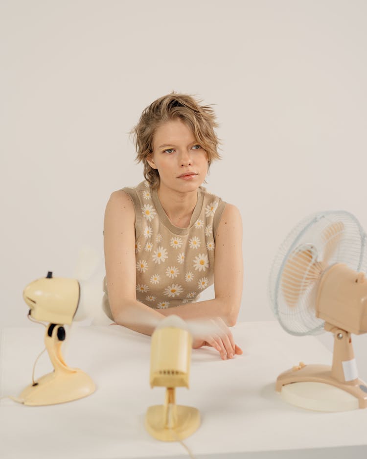 Woman In Floral Tank Top Sitting In Front Of Electric Fans