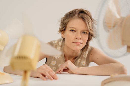 A woman enjoying a calming breeze from fans in a minimal studio backdrop.