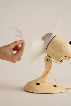 Close-up of a hand holding a feather near a spinning vintage fan in a studio setting.