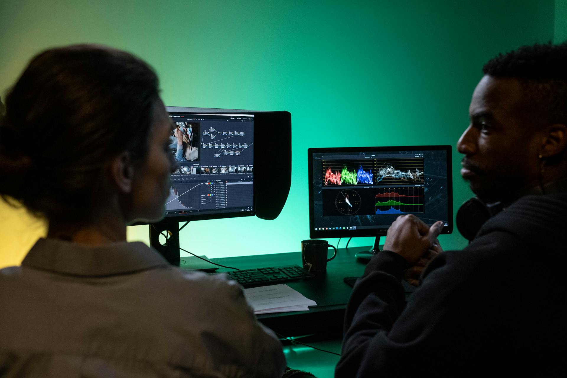 Two colleagues collaborating on video editing, analyzing color grading on dual monitors in a studio.