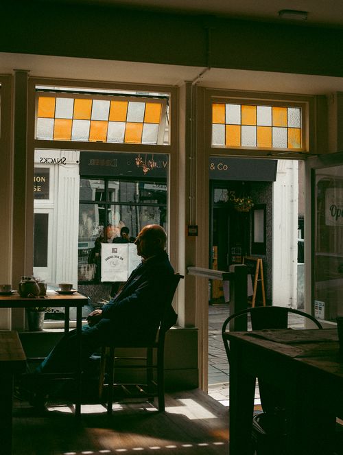 Free Senior man enjoying a quiet moment in a cozy coffee shop, seated by the window with soft natural light. Stock Photo