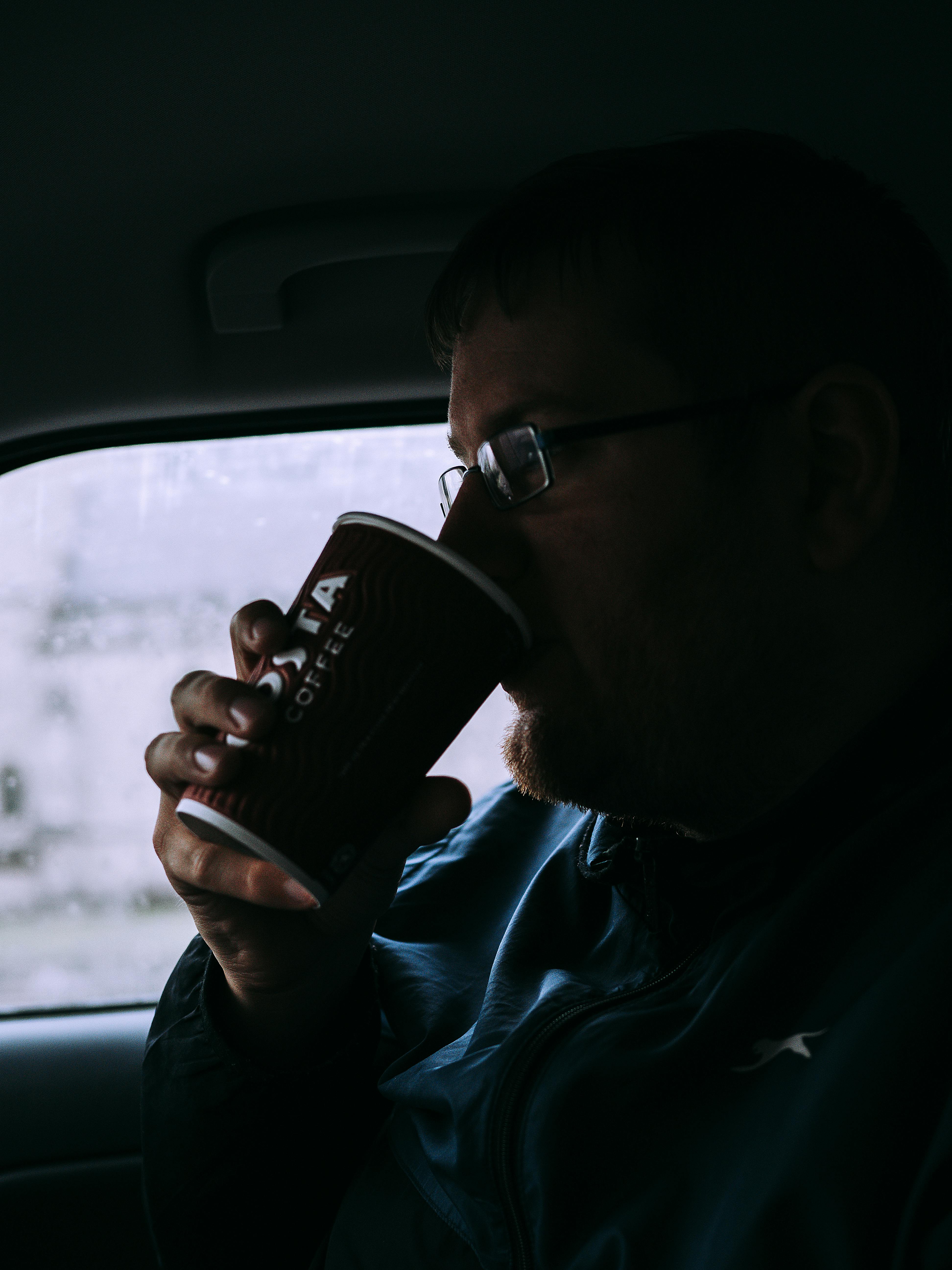 Silhouette of a man drinking coffee inside a car on a rainy day.