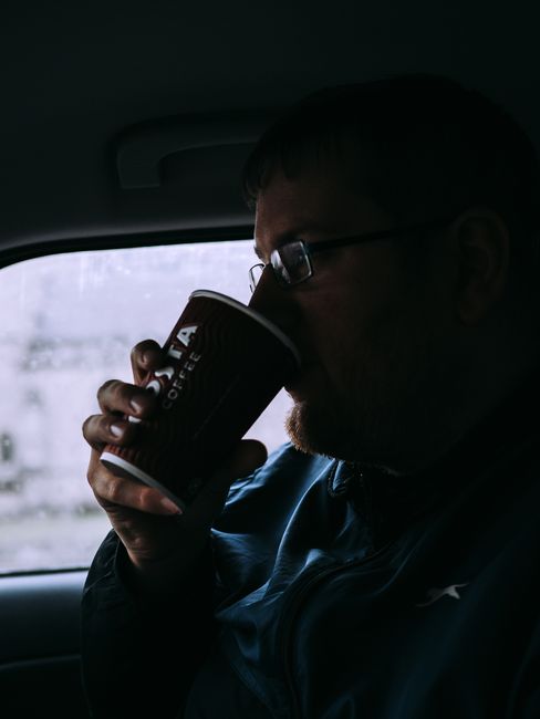 Silhouette of a man drinking coffee inside a car on a rainy day.