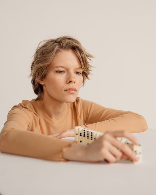 Free A focused woman in a neutral setting playing with dominoes, exuding concentration and calmness. Stock Photo