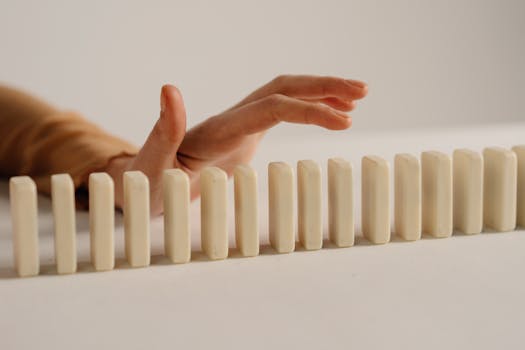 A hand poised to stop falling dominoes, depicting control and intervention.