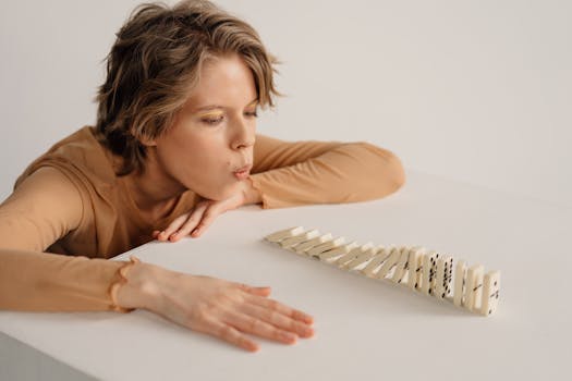 A woman blows on leaning dominoes on a white table indoors.