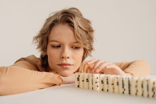 Free A woman attentively watches domino tiles as they lean, creating a chain reaction indoors. Stock Photo