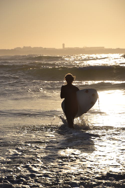 Free A Person Walking on the Beach while Carrying a Surfboard Stock Photo