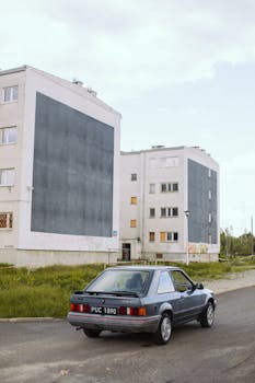 A classic car parked on an urban street, surrounded by residential buildings.