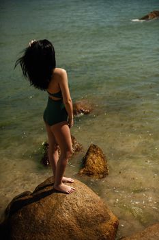 A woman standing on a rock by the sea in Vietnam, gazing at the water.