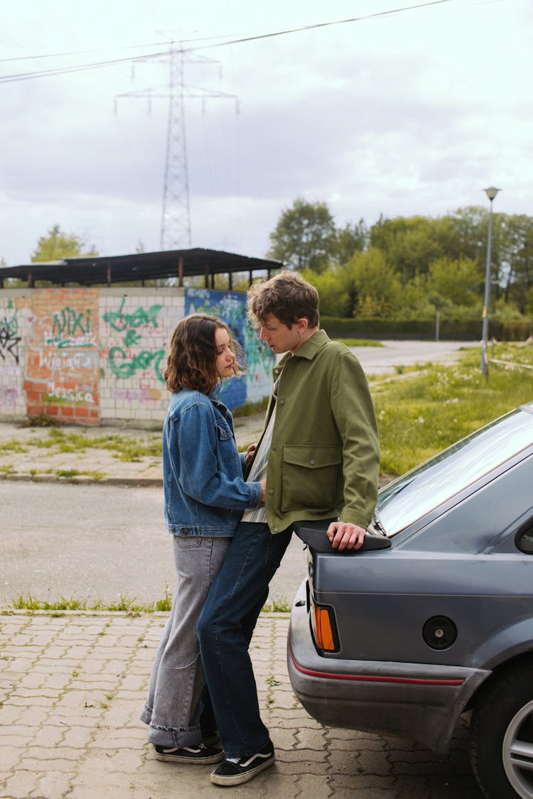 A Couple Standing Together While Leaning On The Car