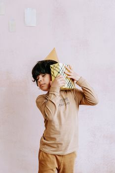 Child wearing party hat holds a plaid wrapped gift, celebrating indoors.