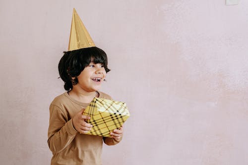 Free A Young Boy in Beige Sweater Smiling while Holding a Gift Stock Photo