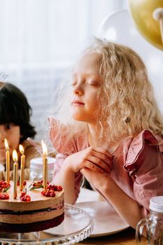 A girl closes her eyes making a wish during a birthday celebration with a decorated cake.