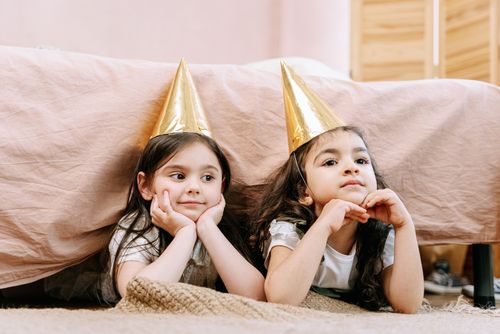 Free Two young girls wearing gold party hats enjoy a birthday celebration indoors. Stock Photo