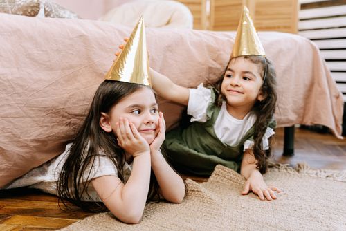 Free Two young girls having fun with party hats indoors. Playful childhood moment captured in a cozy setting. Stock Photo