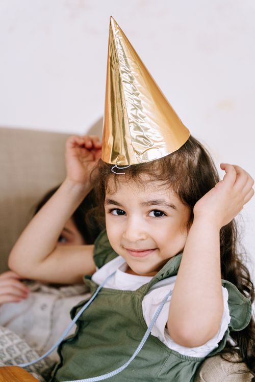 Free Charming young girl in a festive mood with a golden party hat, smiling indoors. Stock Photo