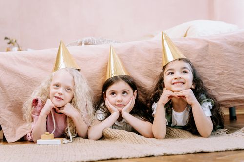 Free Three children in party hats lying on the floor with smiles, enjoying a fun indoor celebration. Stock Photo