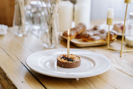 A beautifully arranged dessert with a candle on a ceramic plate, set on a rustic wooden table.