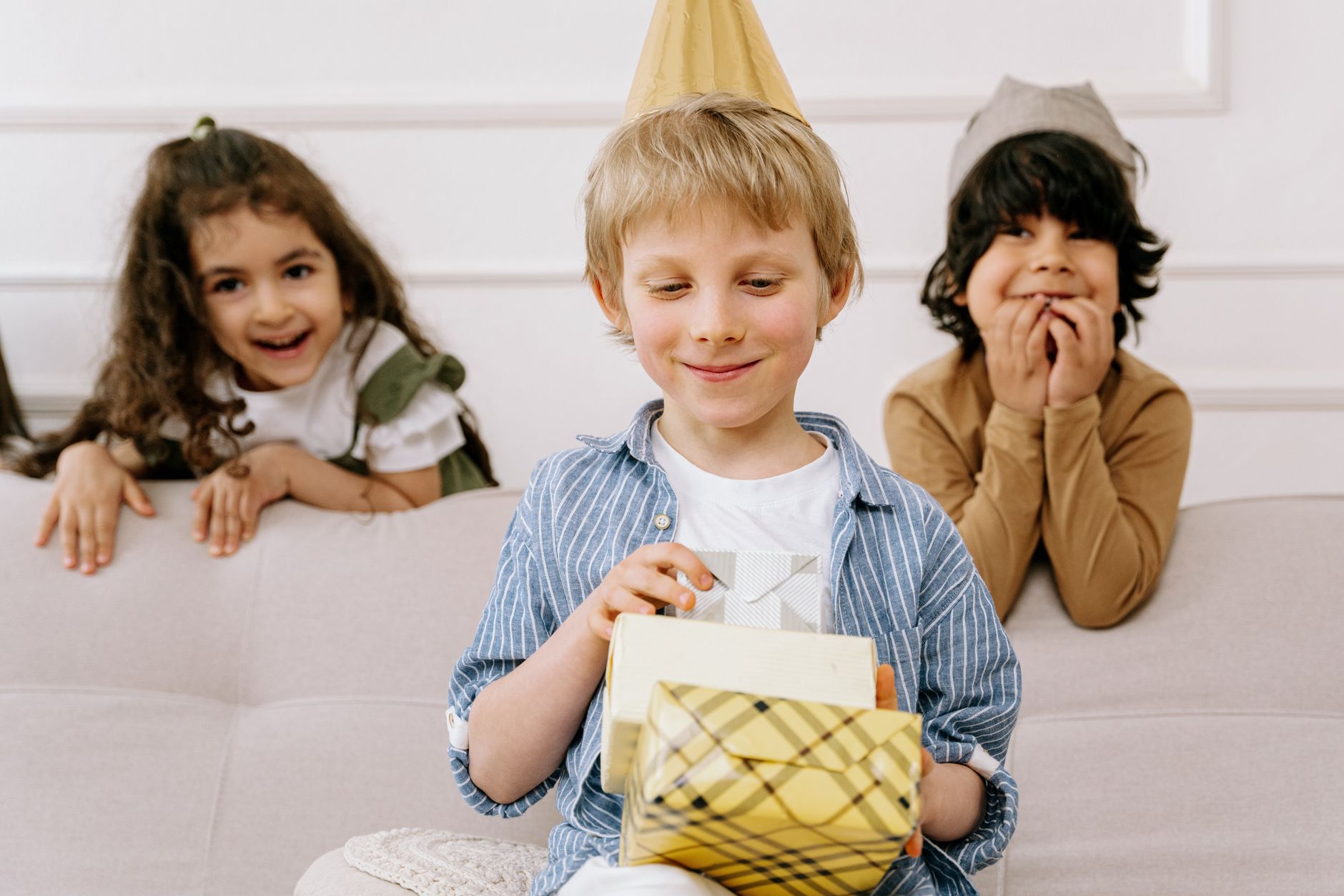 Três crianças sorrindo enquanto abrem presentes em uma festa