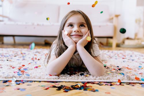Free Adorable child lying on carpet in a confetti-filled room, looking up with a joyful expression. Stock Photo