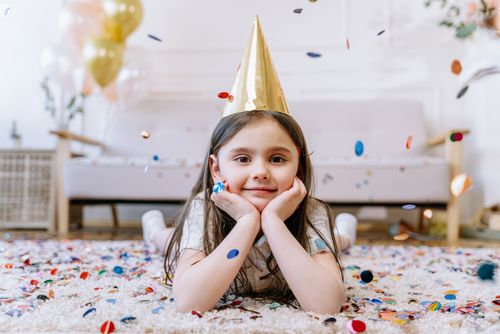 Free A joyful girl at a birthday party lying on the carpet surrounded by confetti. Stock Photo
