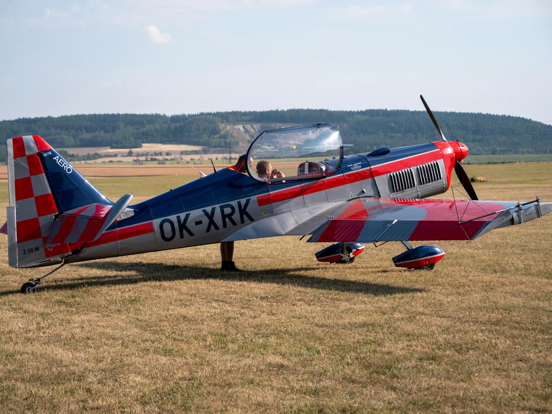 A vibrant aerobatic aircraft on a grassy field in Rakovník, Czechia with a pilot preparing for takeoff.
