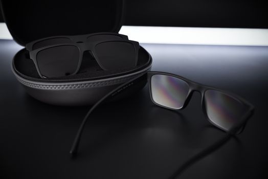 Close-up of black sunglasses and case on a reflective, sleek surface.