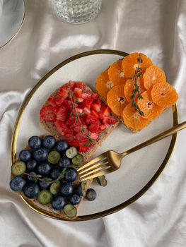Colorful fruit-topped wheat bread slices with strawberries, blueberries, and oranges on a classy plate.
