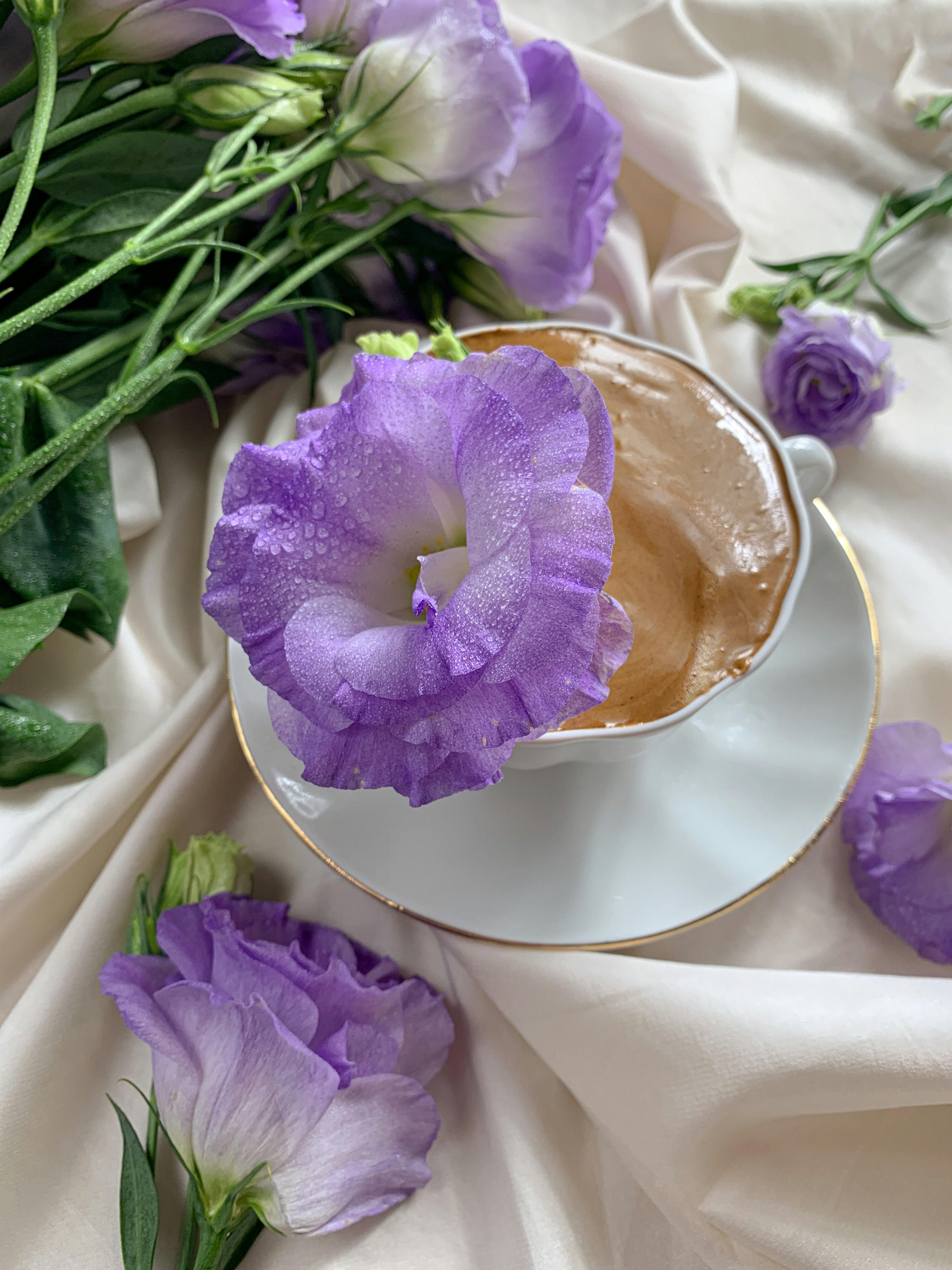 Top view of a dalgona coffee surrounded by purple eustoma flowers on a silk fabric. Elegant and serene setup.