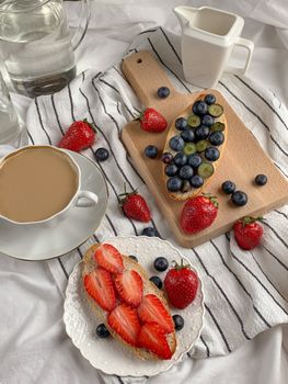 Top view of fruit-topped breakfast toasts with coffee on a striped cloth, styled elegantly.