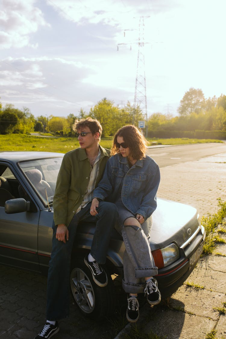 A Couple Sitting On The Car Hood