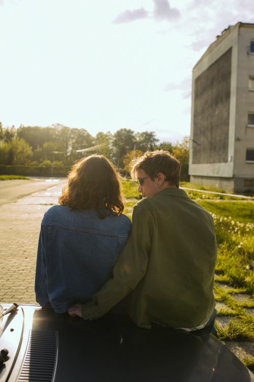 Free Young couple in a loving moment, sitting on a car hood under bright sunlight. Stock Photo