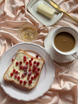 A stylish breakfast arrangement featuring toast with berries and butter, along with a cup of coffee, on satin fabric.