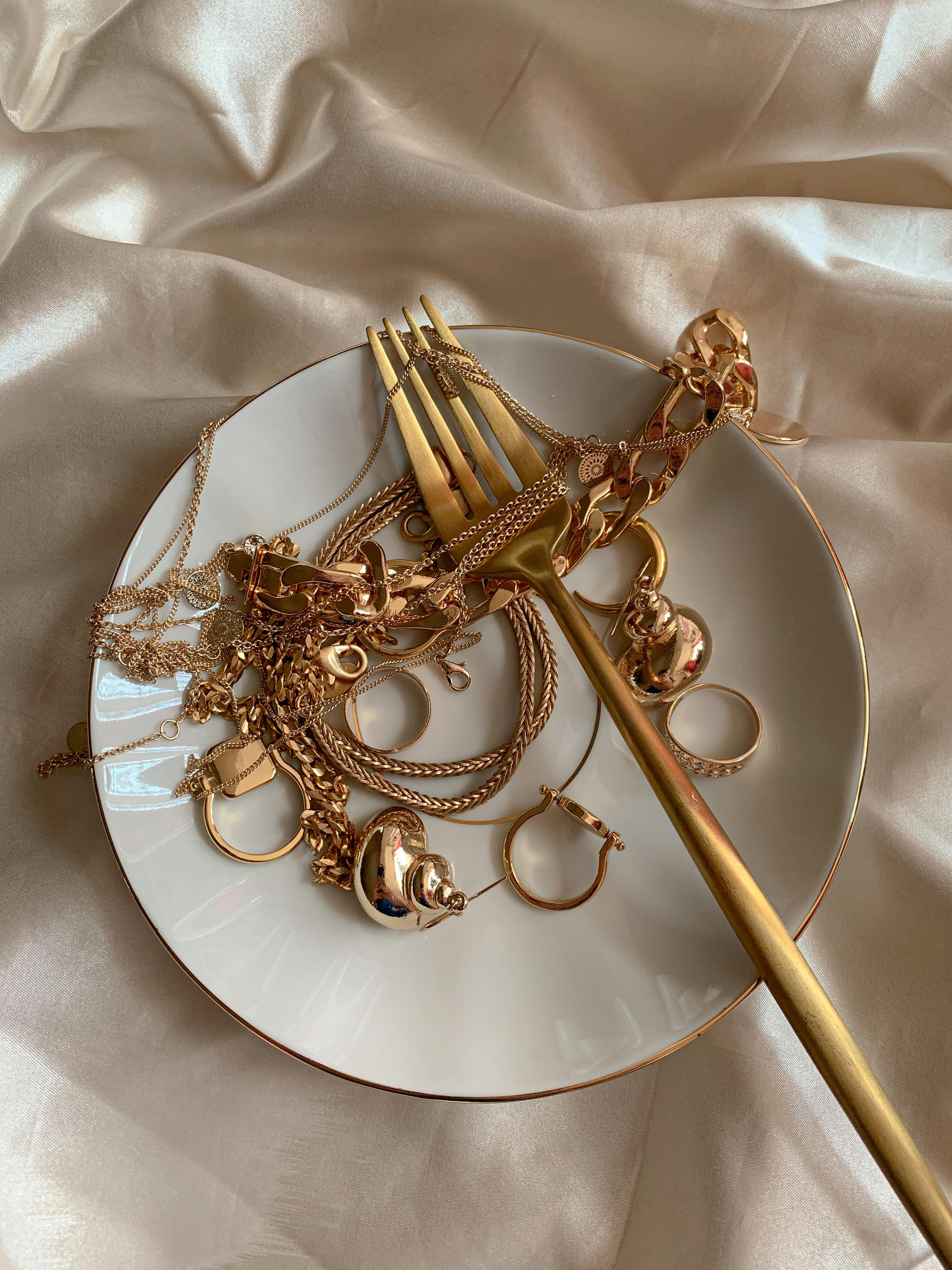 golden jewelry and golden fork on white saucer on beige silk