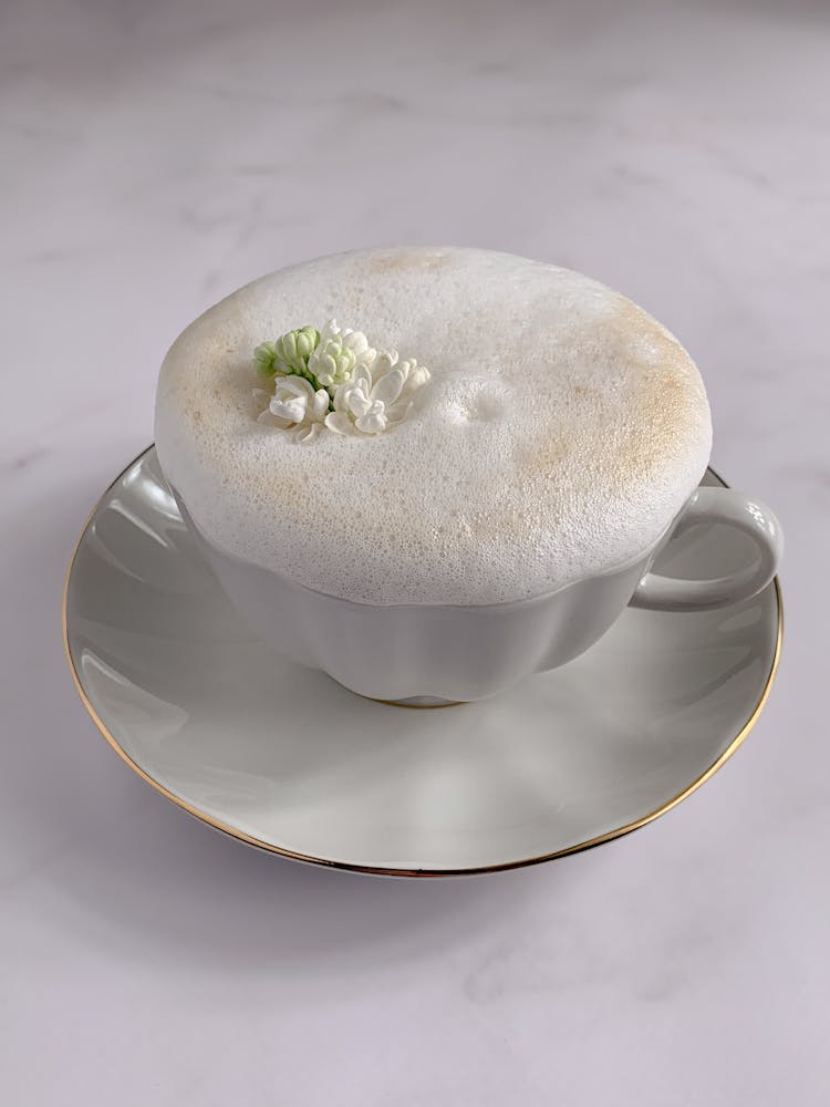 White Flower On White Foamy Coffee In White Porcelain Cup And Saucer