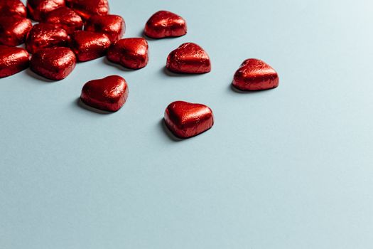 Heart shaped red chocolates scattered on a blue background with copy space.