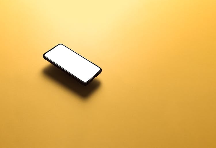 Mobile Phone With White Screen Flowing Above Yellow Background